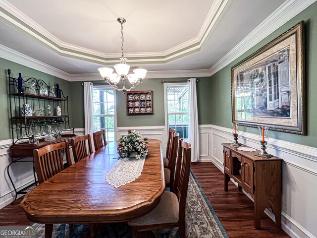 dining area featuring dark wood-type flooring, a raised ceiling, a notable chandelier, and a wealth of natural light