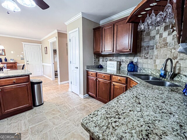 kitchen featuring a sink, ornamental molding, ceiling fan, light stone countertops, and decorative backsplash