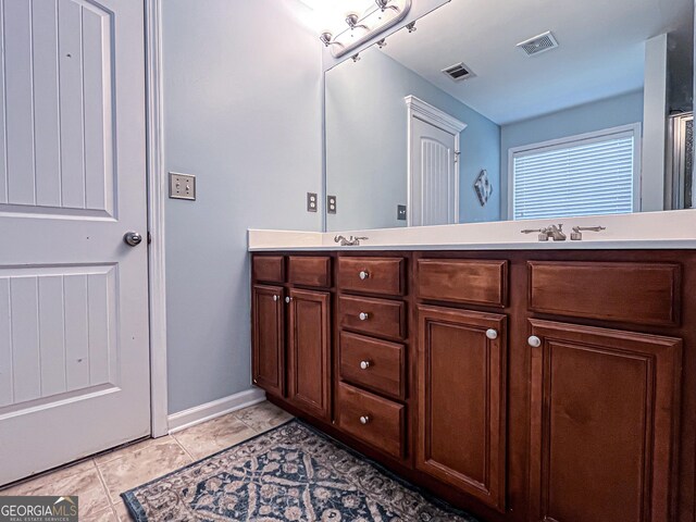 bathroom featuring baseboards, double vanity, a sink, and visible vents