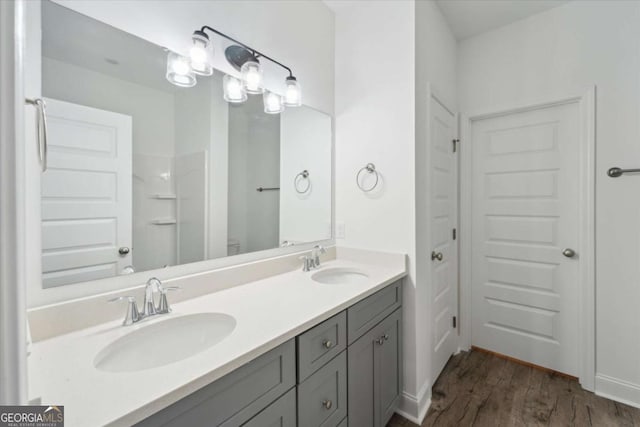 bathroom featuring wood finished floors, double vanity, a sink, and baseboards