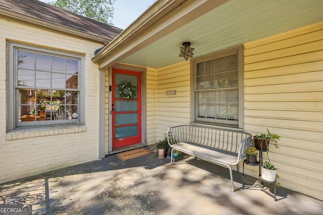 view of exterior entry with a porch, a shingled roof, and brick siding