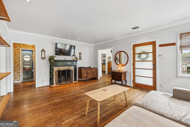 living area featuring crown molding, wood finished floors, visible vents, and a brick fireplace