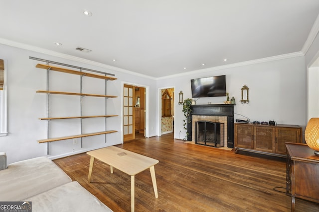 living area featuring a brick fireplace, visible vents, crown molding, and wood finished floors