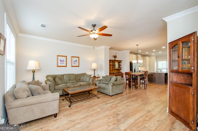 living room featuring light wood-style flooring, crown molding, a ceiling fan, and visible vents