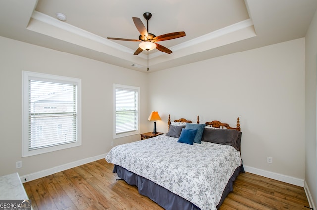 bedroom featuring a tray ceiling, light wood finished floors, baseboards, and visible vents