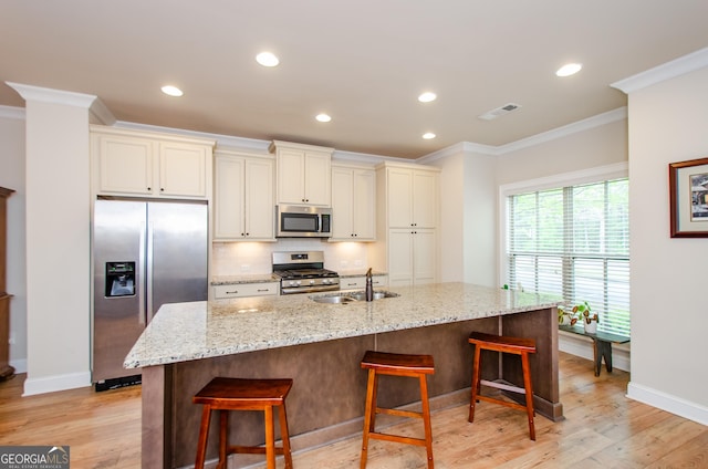 kitchen with baseboards, a sink, light wood-type flooring, appliances with stainless steel finishes, and crown molding
