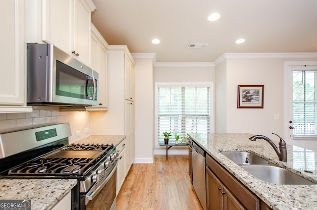 kitchen with visible vents, a sink, ornamental molding, appliances with stainless steel finishes, and light wood-style flooring