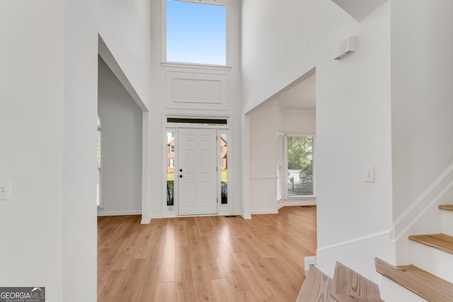 entryway with a towering ceiling, stairs, light wood-type flooring, and baseboards