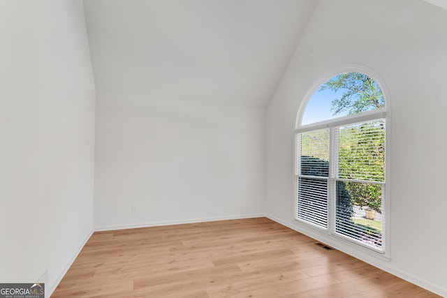 empty room featuring light wood-type flooring, high vaulted ceiling, and baseboards