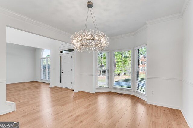 unfurnished dining area with a chandelier, light wood finished floors, ornamental molding, and baseboards