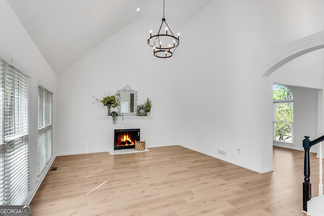 unfurnished living room featuring high vaulted ceiling, a fireplace with flush hearth, light wood finished floors, a chandelier, and arched walkways