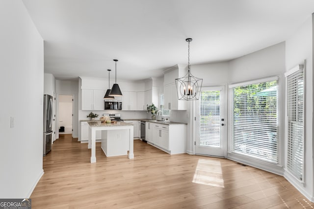 kitchen with stainless steel appliances, a chandelier, white cabinetry, a kitchen island, and light wood-style flooring