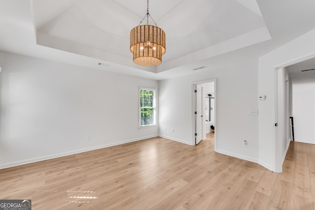 empty room with a tray ceiling, a chandelier, light wood finished floors, and baseboards
