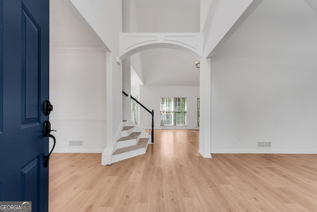 foyer entrance featuring arched walkways, light wood-style floors, a high ceiling, baseboards, and stairway