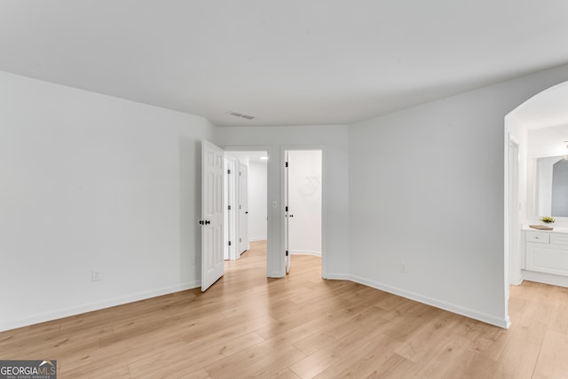 spare room featuring arched walkways, light wood-style floors, and baseboards