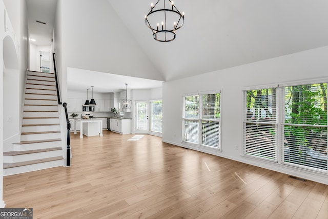 unfurnished living room with a chandelier, high vaulted ceiling, stairs, light wood-type flooring, and baseboards