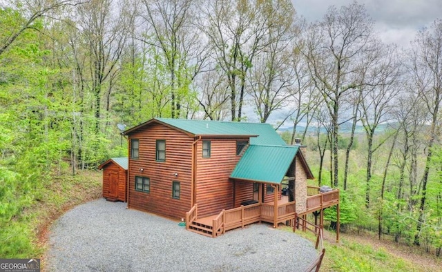 exterior space with a forest view, a wooden deck, metal roof, and a chimney