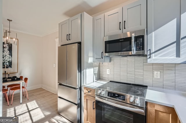 kitchen with baseboards, light countertops, appliances with stainless steel finishes, crown molding, and light wood finished floors
