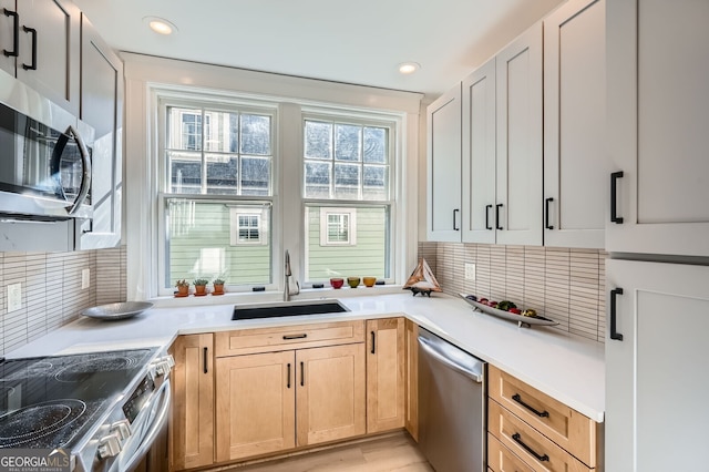 kitchen with light countertops, a sink, backsplash, and appliances with stainless steel finishes