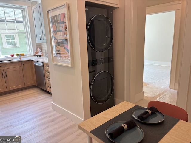 clothes washing area featuring stacked washer / dryer, laundry area, baseboards, and light wood-type flooring