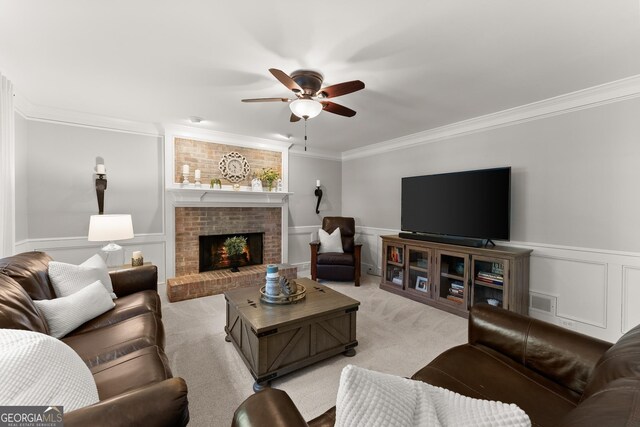 living area with a wainscoted wall, a ceiling fan, light carpet, crown molding, and a fireplace