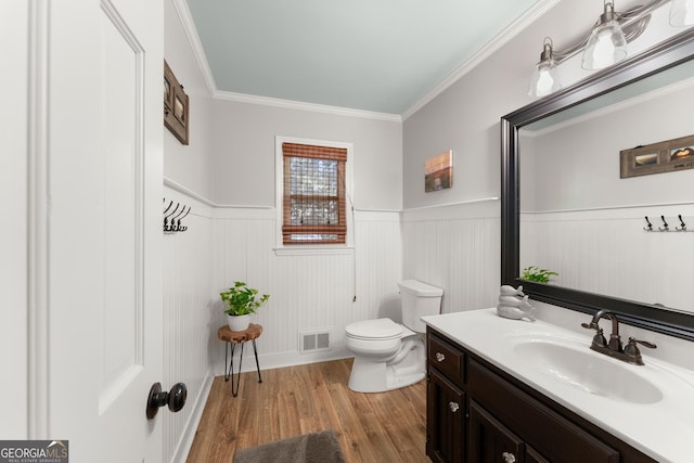 half bathroom featuring a wainscoted wall, wood finished floors, visible vents, toilet, and vanity