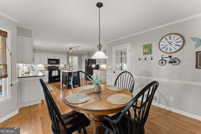 dining space with baseboards, ornamental molding, and light wood-style floors