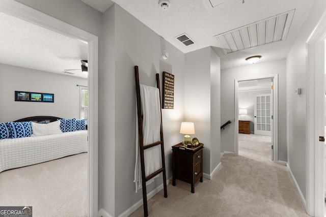 corridor featuring an upstairs landing, baseboards, attic access, a textured ceiling, and light colored carpet