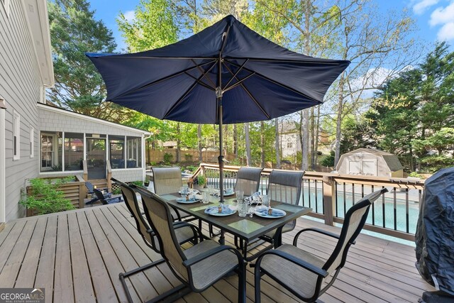 deck with a storage unit, a fenced in pool, a fenced backyard, a sunroom, and outdoor dining area