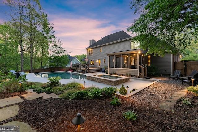 pool at dusk with a wooden deck, a sunroom, an outdoor pool, and fence