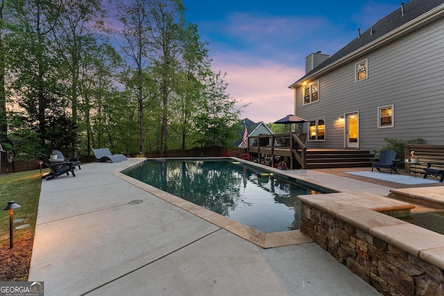pool at dusk with a patio area, an outdoor pool, and a deck