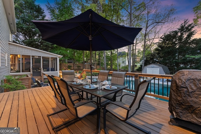 deck featuring a storage unit, a fenced in pool, an outbuilding, outdoor dining space, and a sunroom