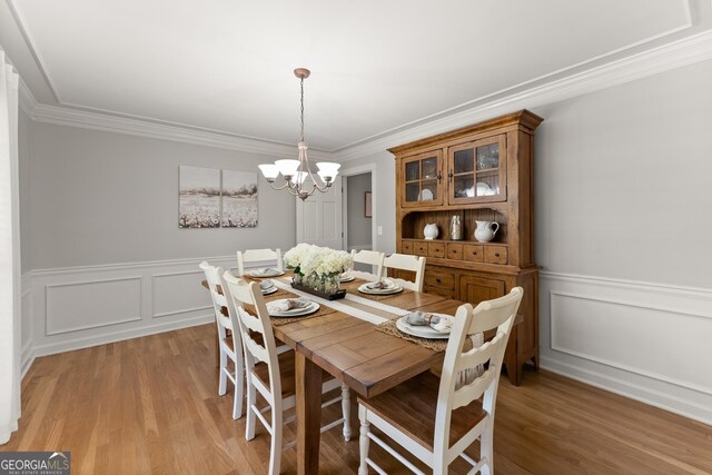 dining room featuring light wood-type flooring, wainscoting, ornamental molding, and an inviting chandelier