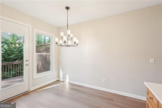 unfurnished dining area with light wood-style flooring, a notable chandelier, and baseboards