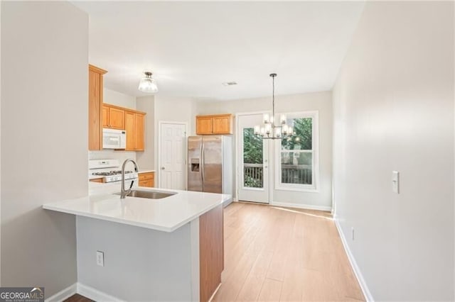 kitchen with a peninsula, a sink, white appliances, and baseboards