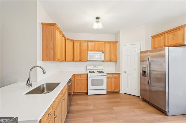 kitchen featuring tasteful backsplash, appliances with stainless steel finishes, light countertops, a sink, and light wood finished floors