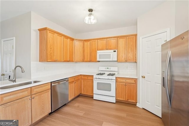 kitchen with light wood-style flooring, tasteful backsplash, appliances with stainless steel finishes, a sink, and light countertops