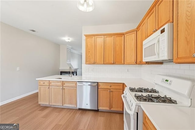 kitchen with a sink, backsplash, white appliances, and light wood-style floors