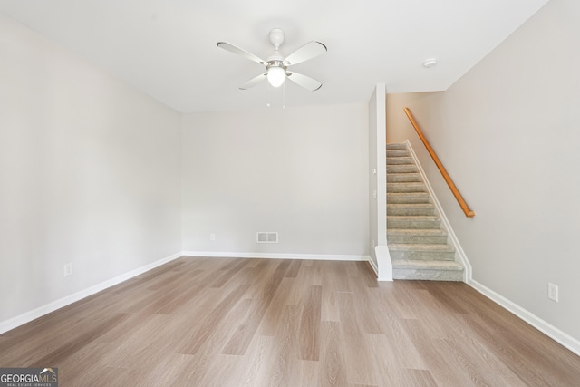 unfurnished living room with light wood-style flooring, a ceiling fan, visible vents, stairway, and baseboards