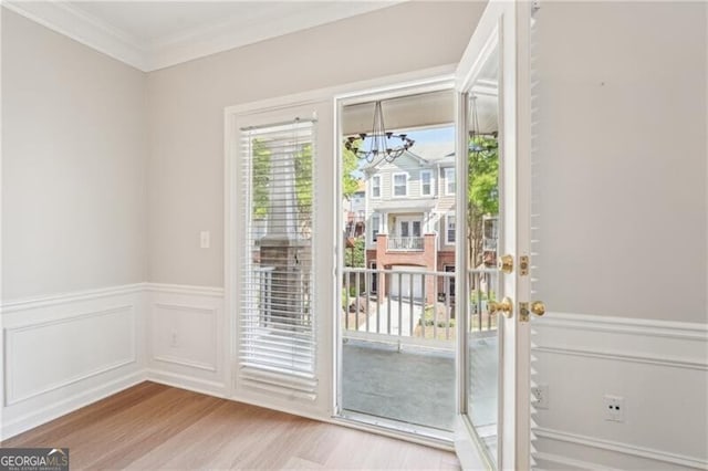 doorway to outside featuring crown molding, a decorative wall, an inviting chandelier, wood finished floors, and wainscoting