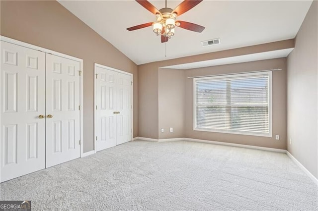 unfurnished bedroom featuring two closets, lofted ceiling, visible vents, and carpet floors