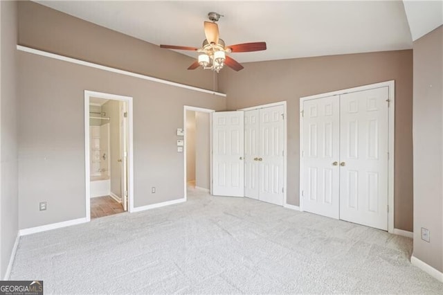 unfurnished bedroom with ensuite bath, carpet flooring, lofted ceiling, multiple closets, and baseboards