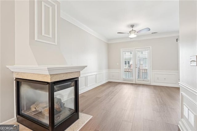 unfurnished living room with wood finished floors, a multi sided fireplace, ornamental molding, and ceiling fan