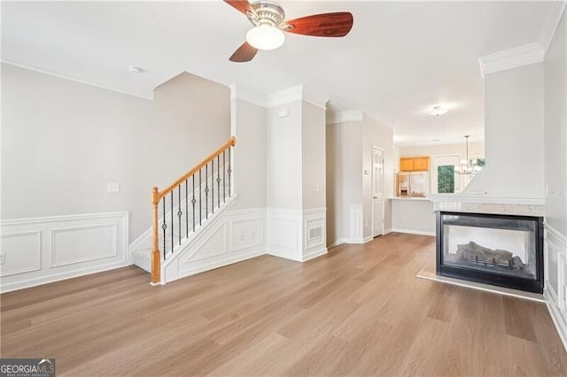 unfurnished living room with a multi sided fireplace, light wood-type flooring, a ceiling fan, crown molding, and stairs