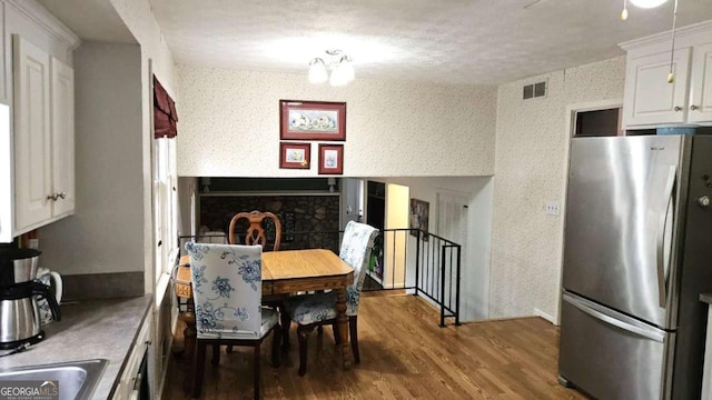 dining space featuring wallpapered walls, a fireplace, a textured ceiling, visible vents, and wood finished floors