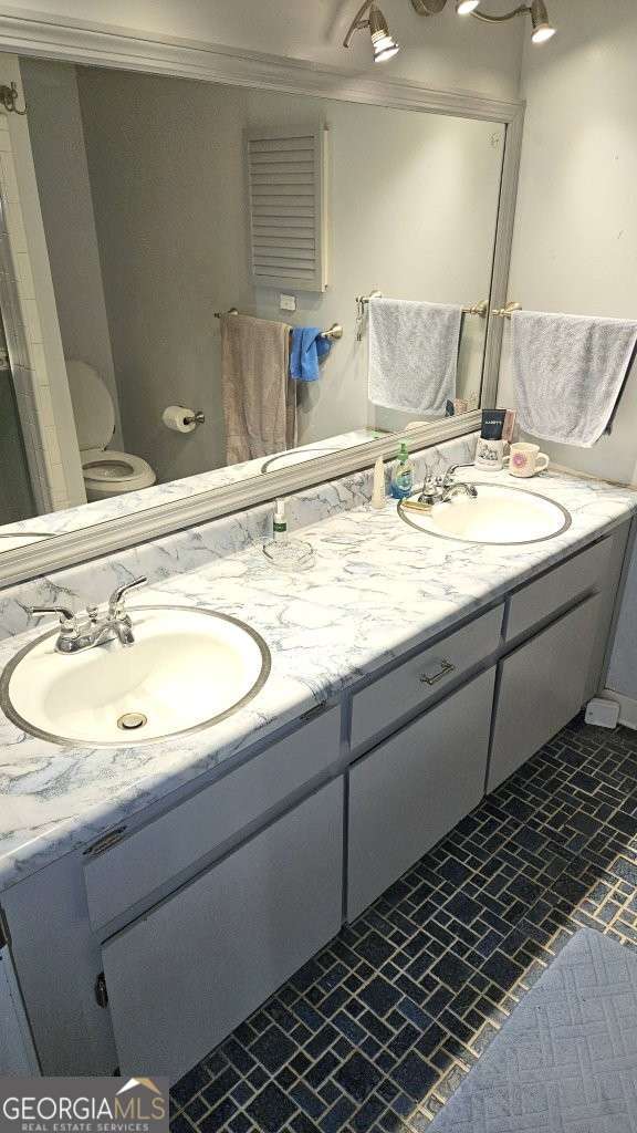 bathroom featuring toilet, double vanity, a sink, and crown molding