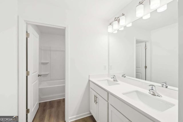 bathroom with wood finished floors, double vanity, a sink, and baseboards