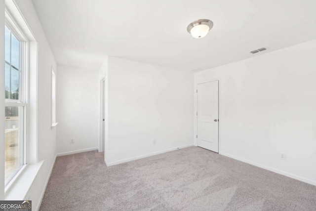 empty room with carpet, visible vents, and baseboards