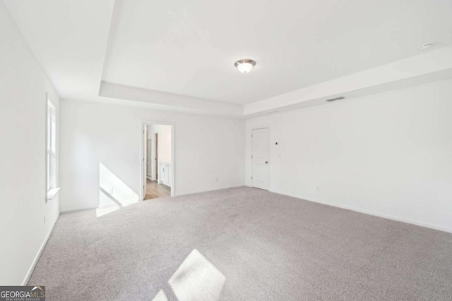 unfurnished room featuring a raised ceiling, visible vents, baseboards, and carpet