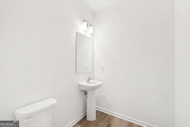 half bathroom with toilet, baseboards, and wood finished floors